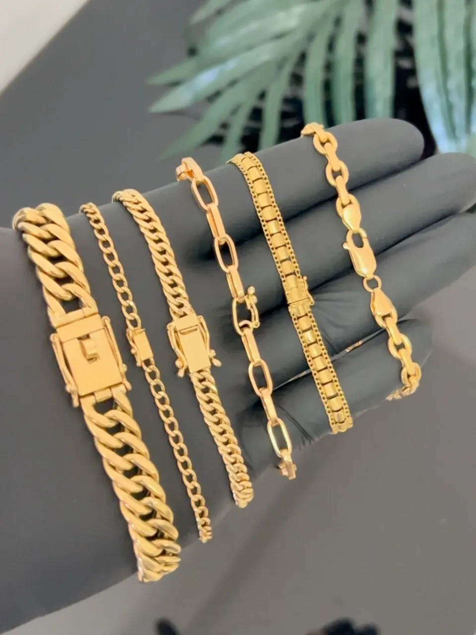 Seis pulseiras em ouro 18k de larguras diferentes sobre luva preta