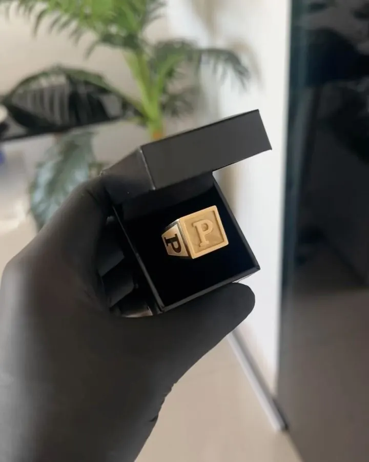 Anel quadrado com letra em ouro 18k no estojo, visto de cima