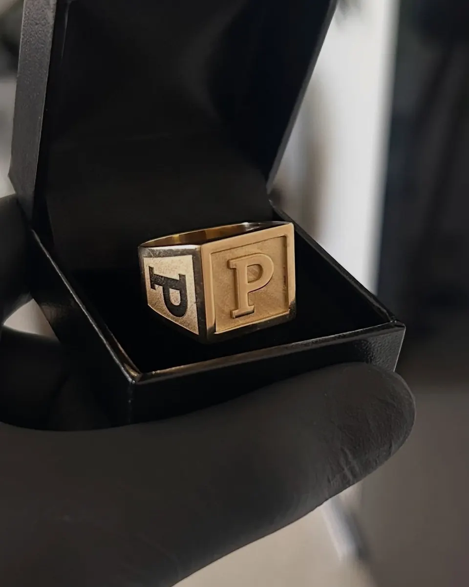 Anel quadrado em ouro 18k com a letra P em relevo, dentro do estojo preto