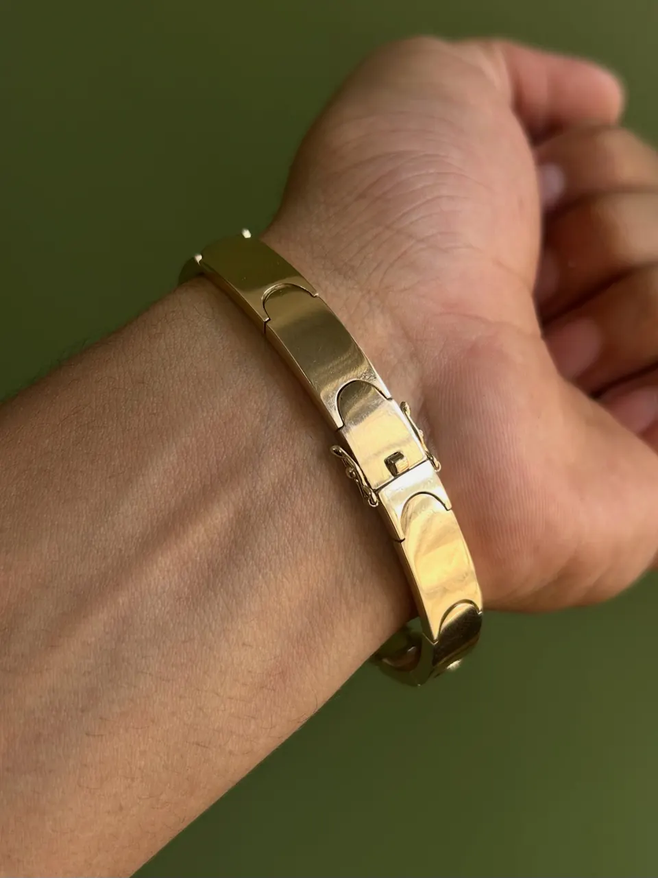 Bracelete liso de 9 mm em ouro 18k no pulso, sobre fundo verde