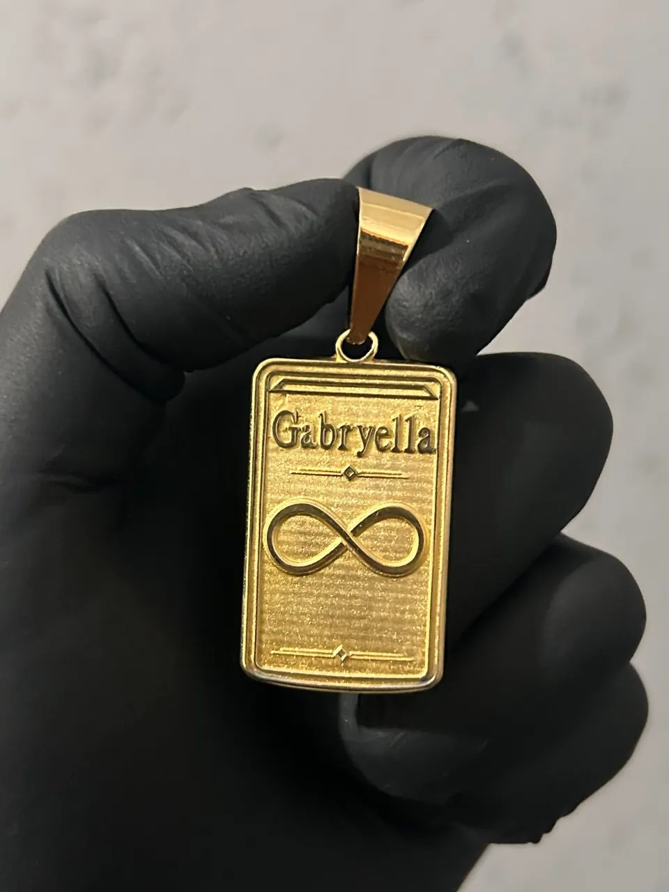 Pingente placa em ouro 18k com o nome Gabryella e o símbolo do infinito em alto relevo